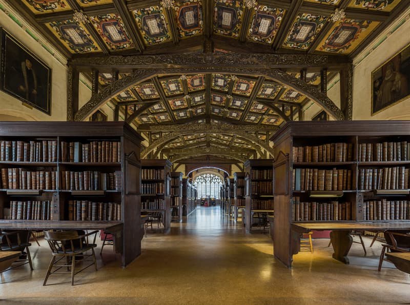 Duke Humfrey's Library at Oxford's Bodleian Library, with rows of medieval bookcases, leaded-glass windows, and reading desks running the length of the room.