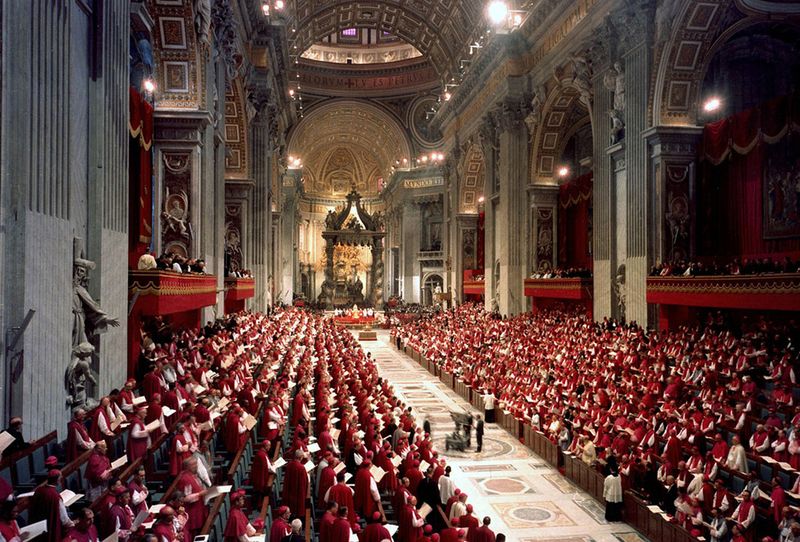A wide interior view of a session of the Second Vatican Council inside St. Peter's Basilica, with hundreds of bishops in red and white vestments seated in long rows facing the altar