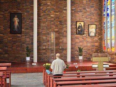 A man kneeling in prayer before the exposed Eucharist during Eucharistic adoration, with a Divine Mercy image to the left and stained glass to the right — the kind of ordinary devotional setting in which indulgenced acts are performed