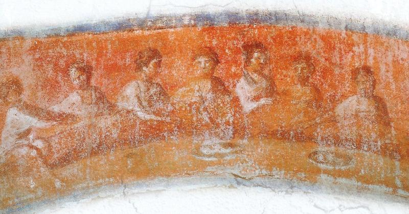 An ancient Roman fresco from the Greek Chapel of the Catacomb of Priscilla showing seven figures reclining on a semicircular couch around a table set with bread and a cup, the figure at the left end reaching forward to break the bread.