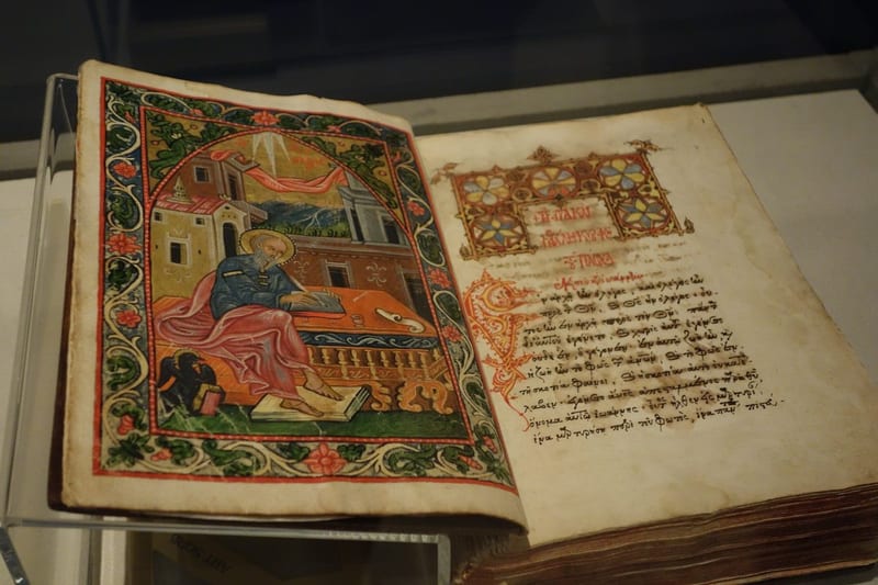 An illuminated medieval Greek manuscript with ornate red lettering and decorative borders on aged parchment, evoking the ancient scriptural tradition behind the Catholic doctrine of biblical inerrancy.