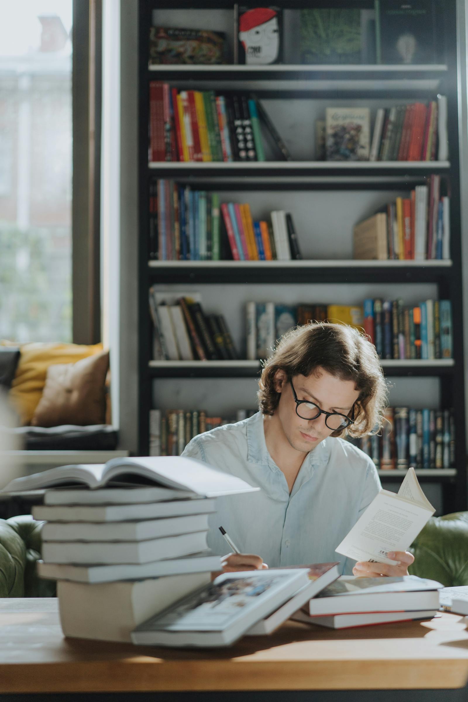Student wearing glasses reading and studying intently at a desk with stacked books and a bookshelf in the background, representing focused academic work and grade preparation