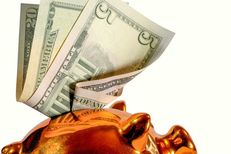 U.S. twenty-dollar bills tucked into a gold piggy bank, evoking long-term college savings