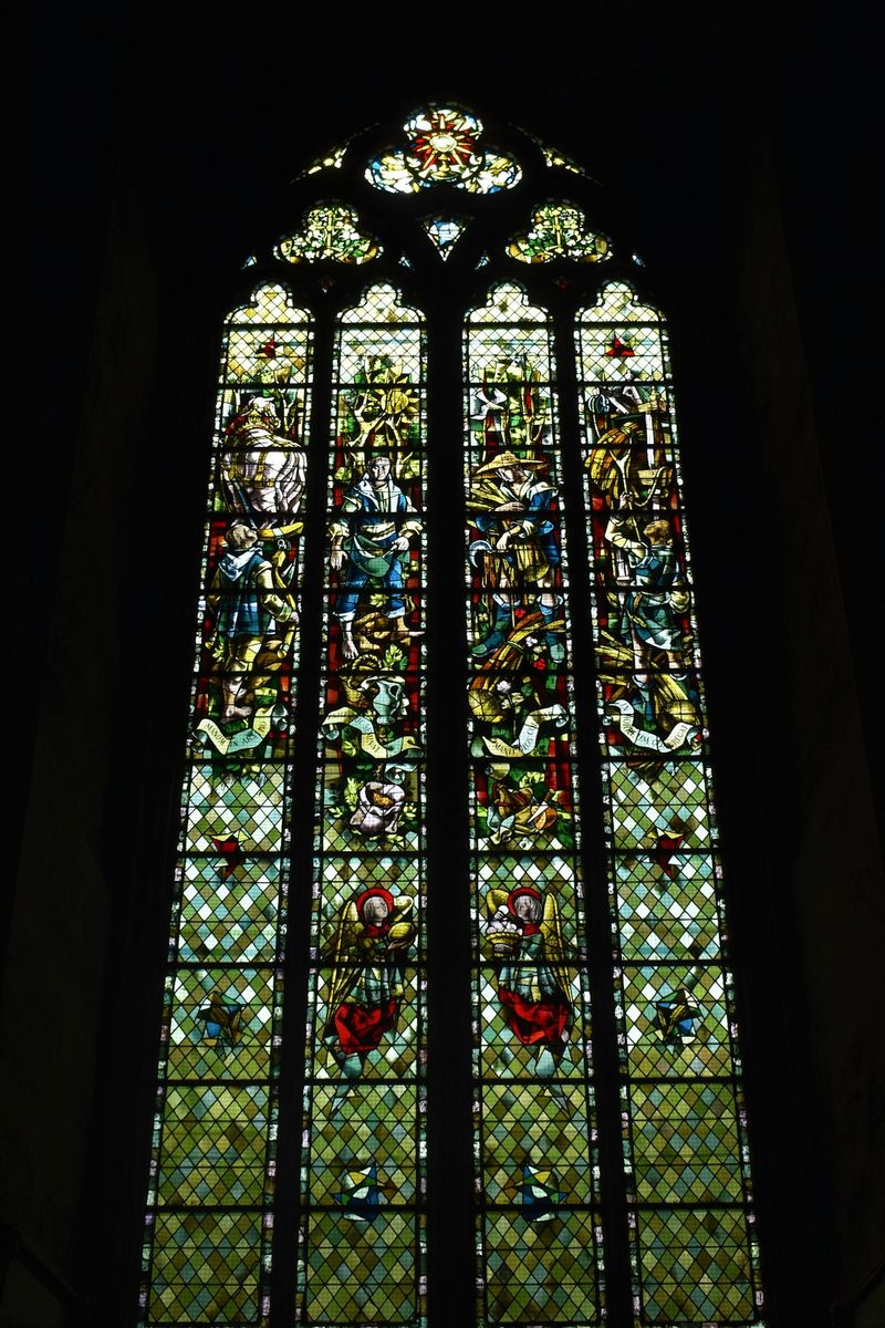A stained glass window in a church depicting biblical scenes, with light streaming through the colored glass