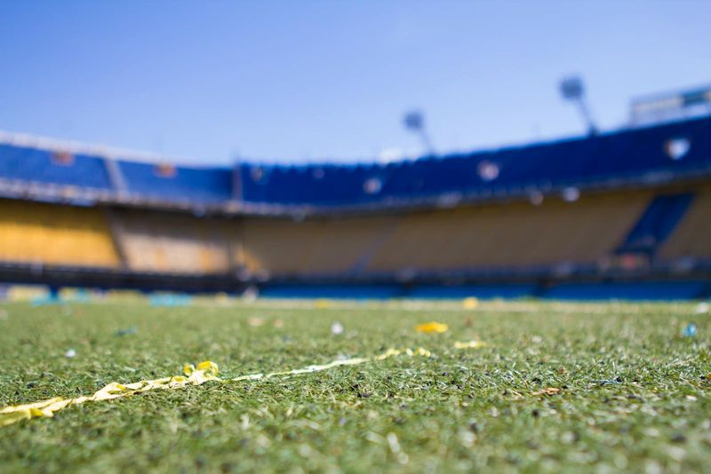 A football stadium field viewed from ground level with bleachers in the background