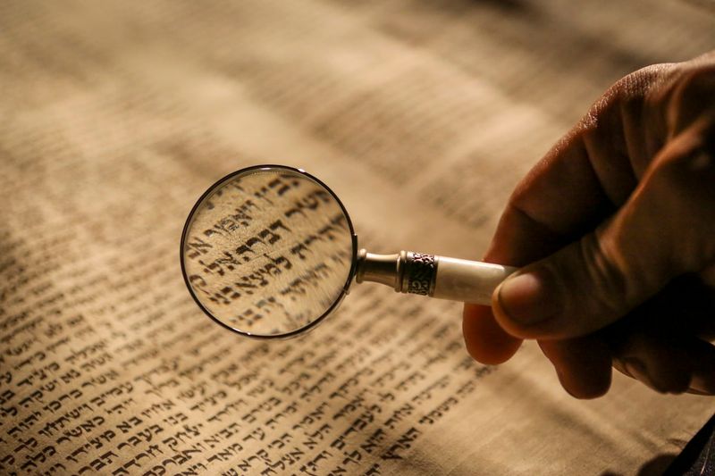 A magnifying glass held over an ancient Hebrew manuscript, revealing the intricate calligraphy of the biblical text