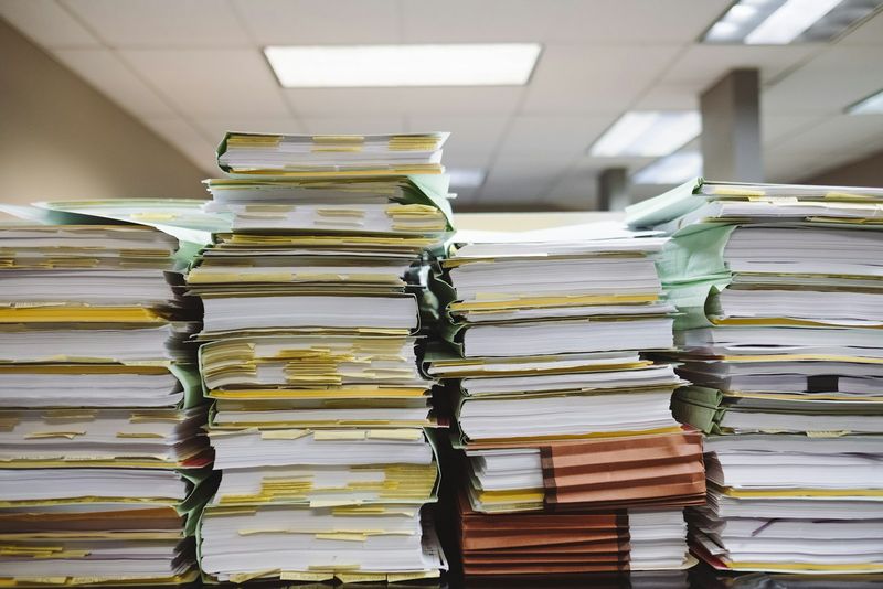 Towering stacks of paperwork and file folders in an office, representing the administrative law block during Week 8 of the Army JAG School