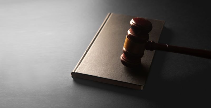 A wooden judge's gavel resting on a leather-bound law book against a dark background