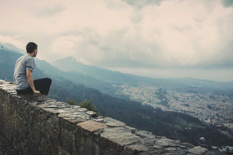A young man sitting on a stone overlook with a sweeping mountain-and-city view in the distance — evocative of an undergraduate at the threshold of his academic future, the kind of moment the Garrett Ham Scholarship is meant to support.