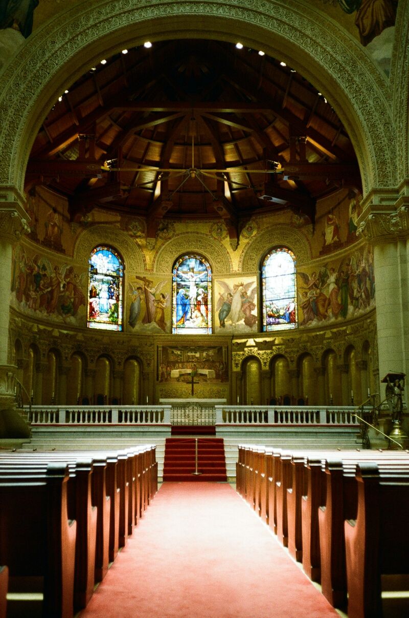 Interior of a grand church with sunlight streaming through stained glass windows and ornate architecture